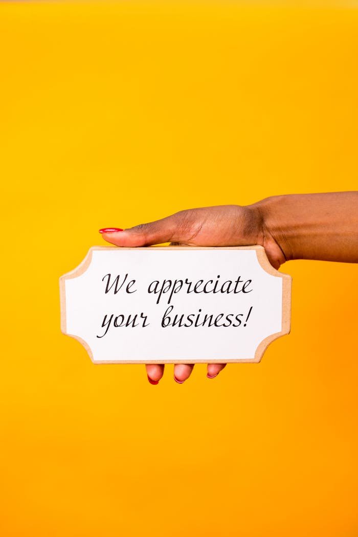A hand holding a sign with We appreciate your business! against a yellow background.